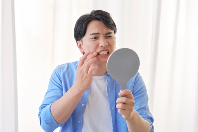 鏡を見て歯に悩む男性